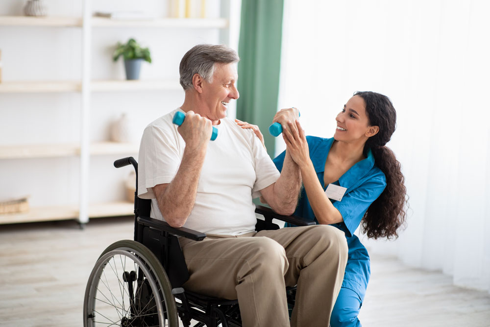 Senior man in wheelchair engaging in exercise with caregiver, using dumbbells in supportive environment, highlighting personalized respite care and activities.